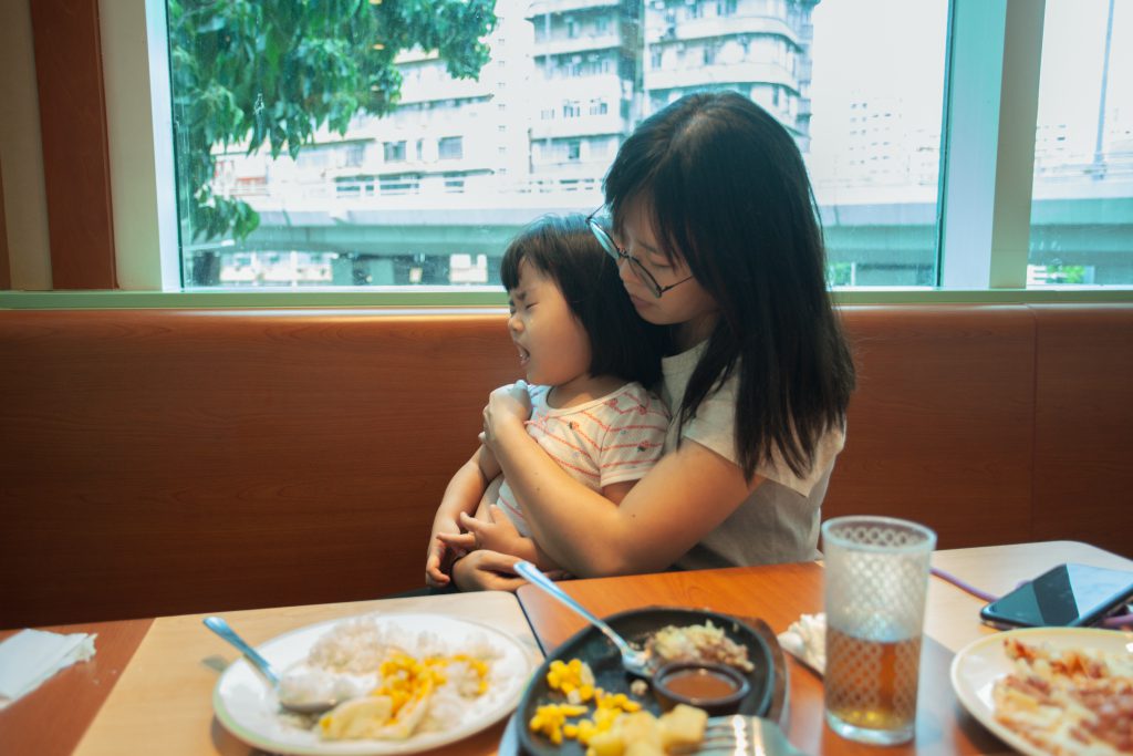一位單親媽媽擁著在餐廳哭喊的女兒，冷靜地安撫她。