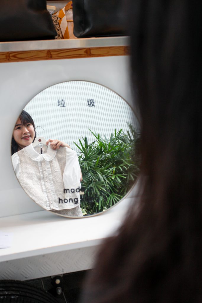 社企Retrovert的鏡子黏有「垃圾，made in Hong Kong」的字樣。一位單親媽媽在工作時照鏡，看中一套適合自己的衣服。